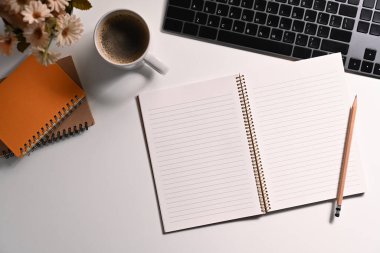 Boş not defteri, kahve fincanı ve kablosuz klavye beyaz ofis masasının üzerinde duruyordu..