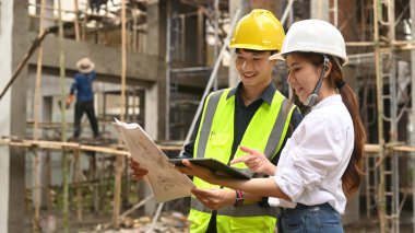 Mühendis ve yöneticiler kasklı inşaat işçisi inşaat alanında plan detaylarını tartışıyorlar..