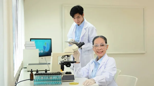 Femme Scientifique Expérimentée Manteau Blanc Assise Devant Microscope Souriant Caméra — Photo