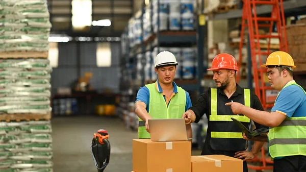 Warehouse workers and manager using laptop in a large warehouse. Manufacture storehouse occupation concept.