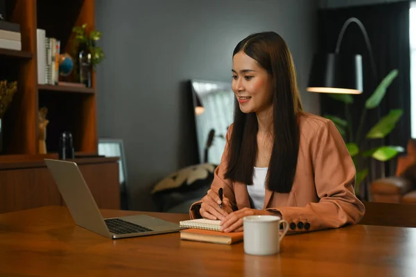 若いアジアの女性のフリーランサーを笑顔オンラインウェビナーを見て ラップトップコンピュータでオンラインで作業 — ストック写真