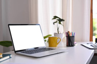 Laptop bilgisayarı, kahve fincanı, saksı bitkisi ve kırtasiyeli beyaz ofis masası. Rahat bir iş yeri.