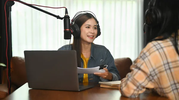 Positive female radio host in headphone streaming live audio podcast from home studio and discussing various topics with her guest.