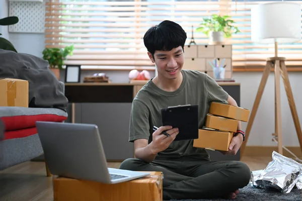 Young man online seller working in home office, preparing parcel boxes of product for delivery. Online selling, e-commerce concept.