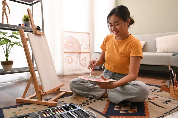 Creative woman painting picture on canvas with oil paints in bright home studio. Leisure activity, creative hobby and art concept.