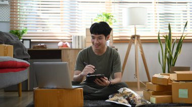 Gülümseyen genç şirket sahibi dizüstü bilgisayardaki siparişi kontrol ediyor ya da kabul ediyor. Çevrimiçi satış. E-ticaret. Çevrimiçi Alışveriş.