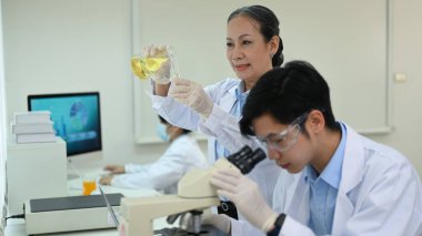 Beyaz önlüklü kıdemli kadın bilim adamı laboratuarda örnekler ve sıvıyı inceliyor. Tıp ve bilim kavramları araştırıyor.