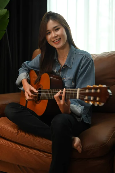 매력적 여자가 소파에서 기타를 연주하고 주말에는 집에서 여가를 보낸다 — 스톡 사진