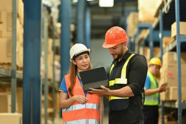 Güvenlik kasketi takan depo işçileri paketlenmiş kutu ve mallarla dolu bir mağazada çalışıyorlar..