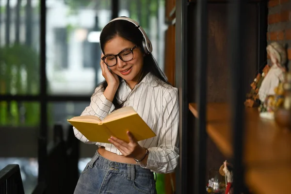 Kütüphanede Kulaklık Takan Kitap Okuyan Olumlu Genç Bir Kadın Halk — Stok fotoğraf