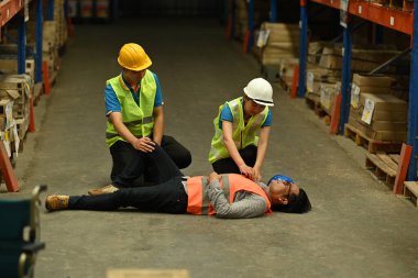 Beton zeminde baygın yatan bir depo çalışanı, iş arkadaşları yaralılara yardım ediyor ve onlara ilk yardımı yapıyor..