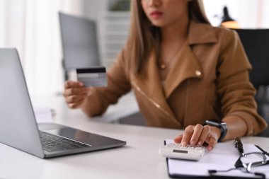 Genç bir kadın, hesap makinesi kullanıyor ve internetten ödeme yapıyor. Çevrimiçi alışveriş, e-ticaret kavramı.