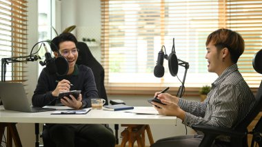 Yoğunlaştırıcı mikrofon kullanan iki mutlu podcaster ev stüdyosundan podcast kaydediyor. Radyo, podcast ve teknoloji konsepti. 