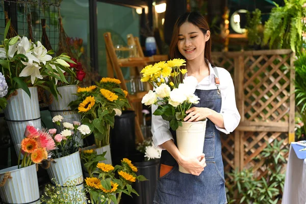 成功した若い女性花屋身に着けていますエプロン保持鍋で新鮮な花とともに彼女の花店の外に立って — ストック写真