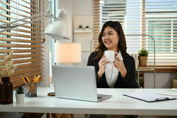 Χαμογελώντας Νεαρή Επιχειρηματίας Κάθεται Στο Γραφείο Της Πίνοντας Καφέ Και — Φωτογραφία Αρχείου