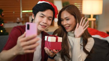 Güzel genç çift cep telefonu kullanıyor ve dekore edilmiş odada selfie çekiyorlar. Tatiller, kutlamalar ve insanlar konsepti.