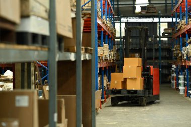 Forklift kamyonu, karton kutularla dolu raflarla dolu büyük bir lojistik dağıtım deposuna park ediyor..