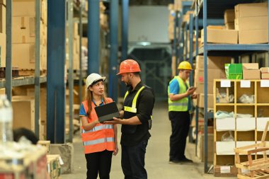 İki depo işçisi raflarla dolu perakende deposu arasında duruyorlar ve tabletteki sipariş detaylarını kontrol ediyorlar..