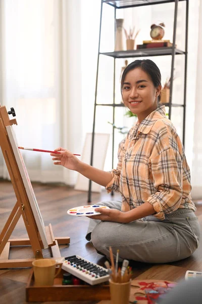 居心地の良いホームスタジオで油絵具でキャンバス上のパレットや絵を保持する女性アーティストの肖像画 — ストック写真