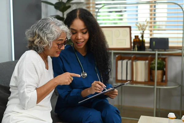 Caring female doctor pointing on digital tablet and explaining medicine dosage to elderly woman. Home health care service concept.