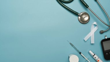 Düz stetoskop, glikoz ölçer, tükenmez kalem, insülin ve şırınga mavi arka planda. Diyabet ve sağlık konsepti.