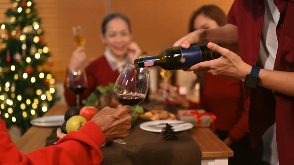 Man pouring wine to father, family celebrating Christmas, thanksgiving party in dining room. Celebration and holidays concept.