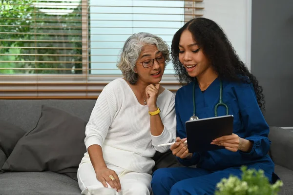 Female doctor holding digital tablet and explaining medicine dosage to elder woman. Home health care service concept.