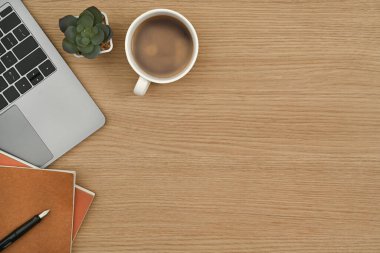 Düz yatak, bir fincan kahve, dizüstü bilgisayar, defter ve ahşap ofis masasında sulu bitki. Kopyalama alanı olan üst görünüm.