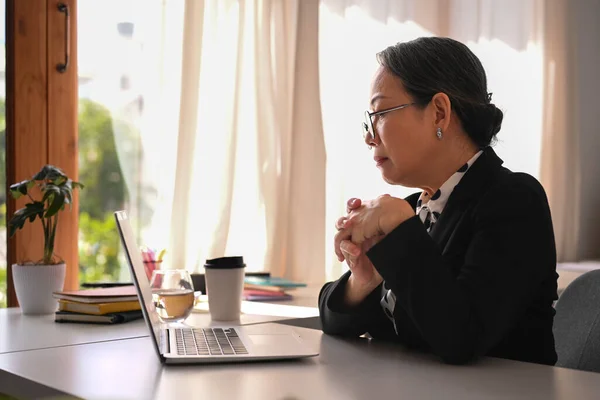 Thoughtful middle age female executive manager reading business email on her laptop computer in the morning.