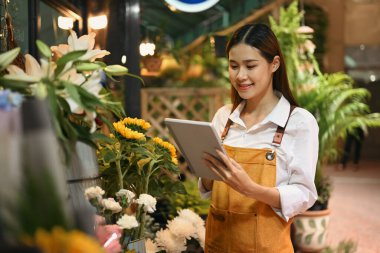 Memnun bayan çiçekçi kontrol ediyor, dijital tabletten online sipariş alıyor. Çiçekçilik, iş ve teknoloji konsepti.