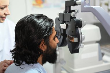 Hintli adamın yan görünüşü, göz görüşünü floropter görüş ölçüm makinesiyle kontrol ediyor..