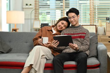 Genç çift internette dijital tablette geziniyor, rahat evlerinde kanepede dinleniyorlar. İnsanlar ve teknoloji kavramı.