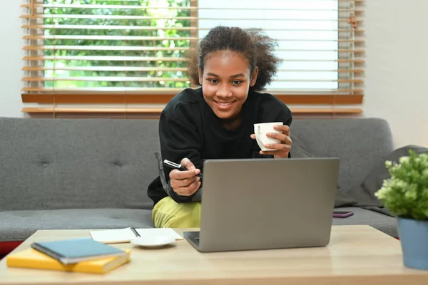 Happy teenage woman relaxing on couch and watching movie or surfing internet on laptop computer.