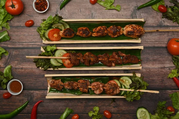 木製の背景に新鮮な野菜と竹のバレルプレートで提供されるグリル肉串焼き — ストック写真