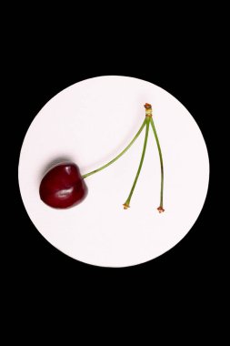 Olgunlaşmış kirazlar, siyah arka planda beyaz bir dairede yakın plan.