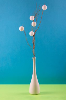 Dal ve beyaz toplarla dolu beyaz bir vazoda, renkli bir arka planda.