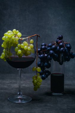 Kırmızı şarap kadehleri ve koyu arkaplanda üzüm demetleri.