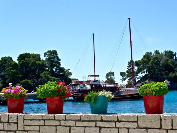 Bloempot op stenen muur met zee en boot in achtergrond — Stockfoto