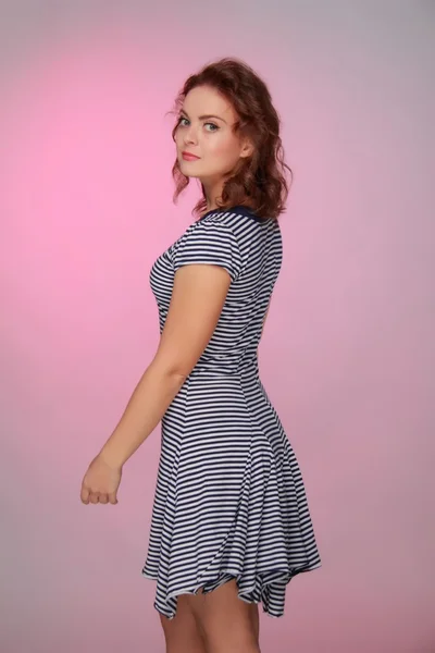 Schöne Frau in einem gestreiften Kleid auf rosa Hintergrund — Stockfoto