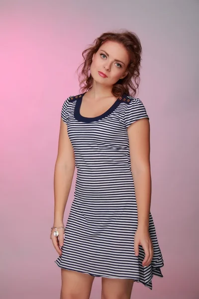 Beautiful woman in a striped dress on pink background — Stock Photo, Image