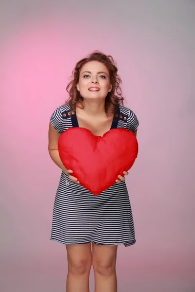 Beautiful woman in a striped dress holding a big heart — Stock Photo, Image