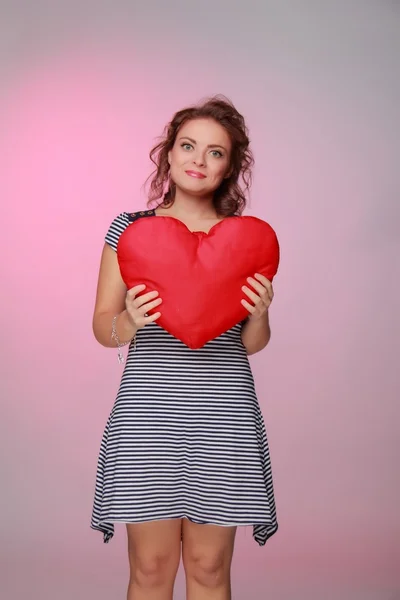 Beautiful woman in a striped dress holding a big heart — Stock Photo, Image