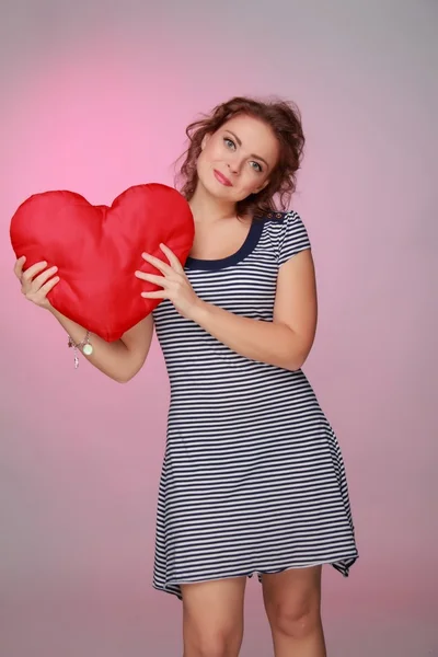 Beautiful woman in a striped dress holding a big heart — Stock Photo, Image