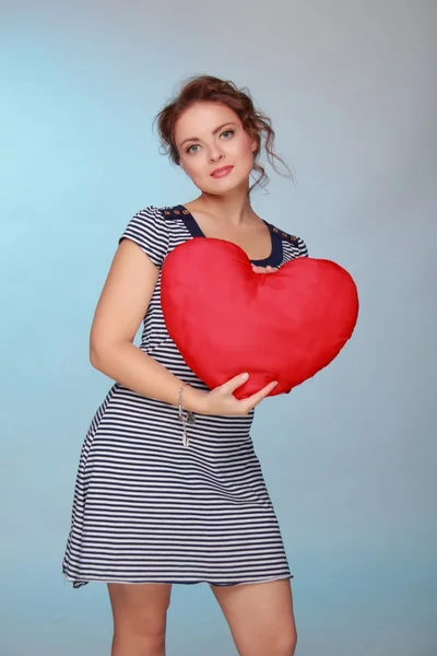 Beautiful woman in a striped dress holding a big heart — Stock Photo, Image