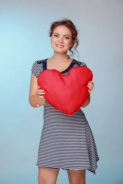 Beautiful woman in a striped dress holding a big heart — Stock Photo, Image