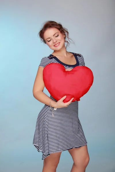 Beautiful woman in a striped dress holding a big heart — Stock Photo, Image