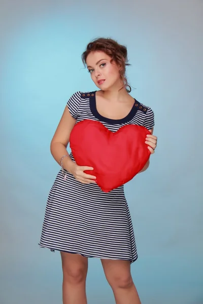 Beautiful woman in a striped dress holding a big heart — Stock Photo, Image