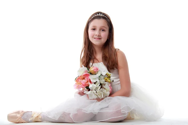 Young ballerina sitting in ballet position holding the flowers — Stock Photo, Image