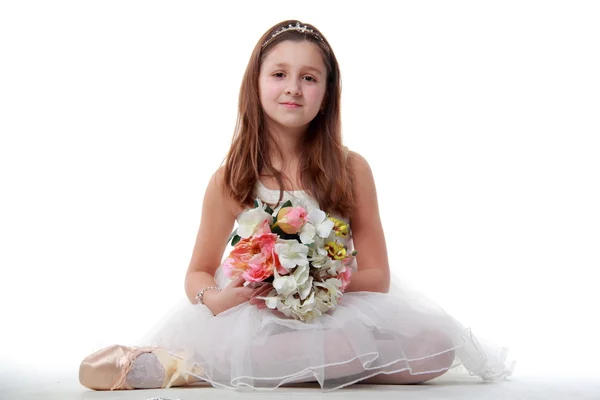 Young ballerina sitting in ballet position holding the flowers — Stock Photo, Image