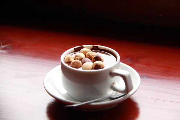 Ζεστή σοκολάτα με ξηρούς καρπούς, σε ένα λευκό φλιτζάνι σε ένα καφέ τραπέζι — Φωτογραφία Αρχείου